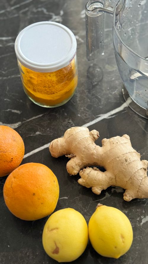 Jus de citron et fruits: citrons, prunes jaunes et gingembre frais sur plan de travail, pot de miel et pichet d’eau à côté. Remède digestion citron.