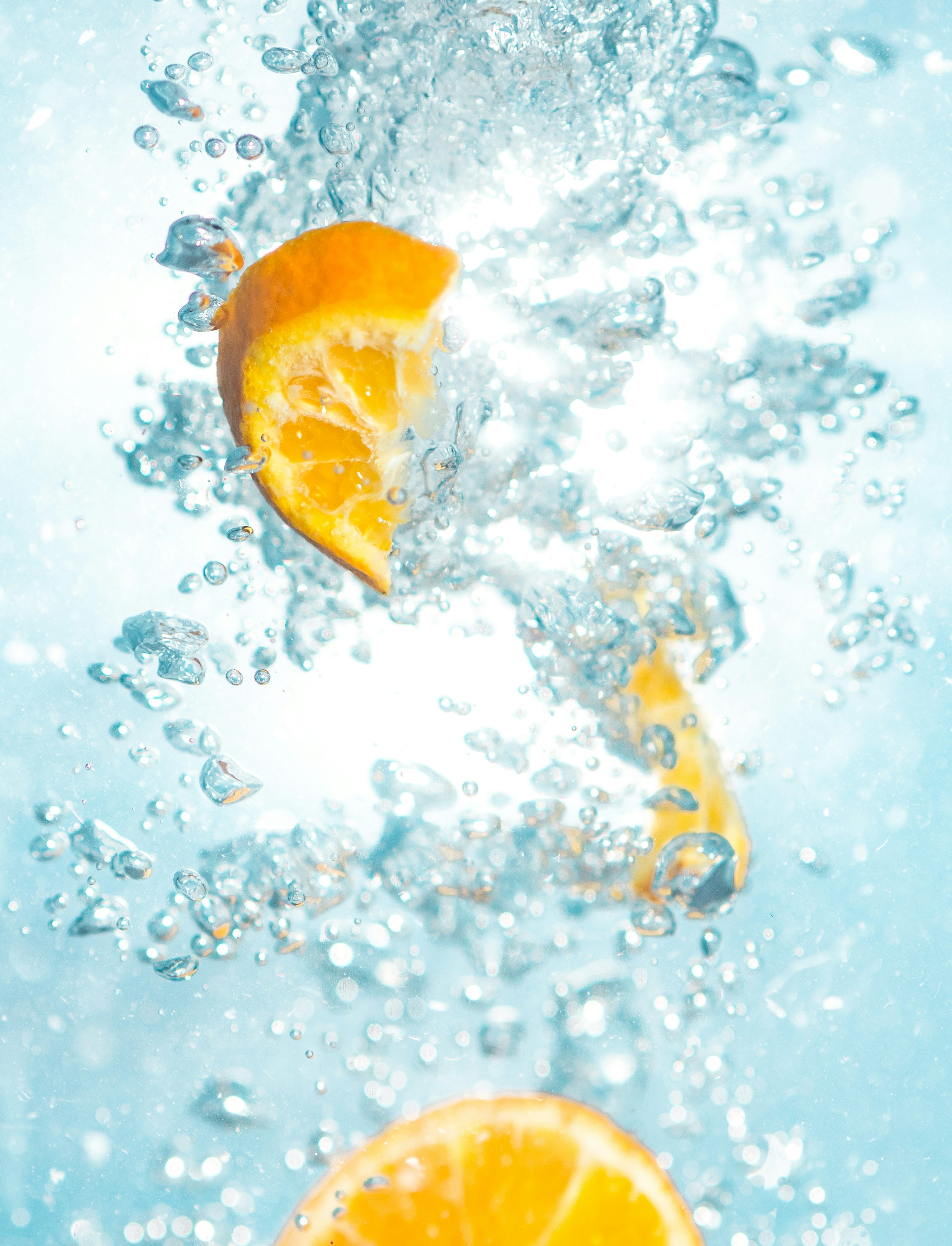 Tranche d’orange pressée dans de l’eau pétillante, éclaboussures et bulles autour, évoquant un remède digestion citron.